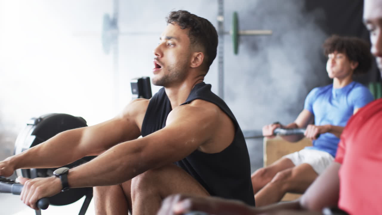 Strong, fit biracial male training on rowing machine in black tank top