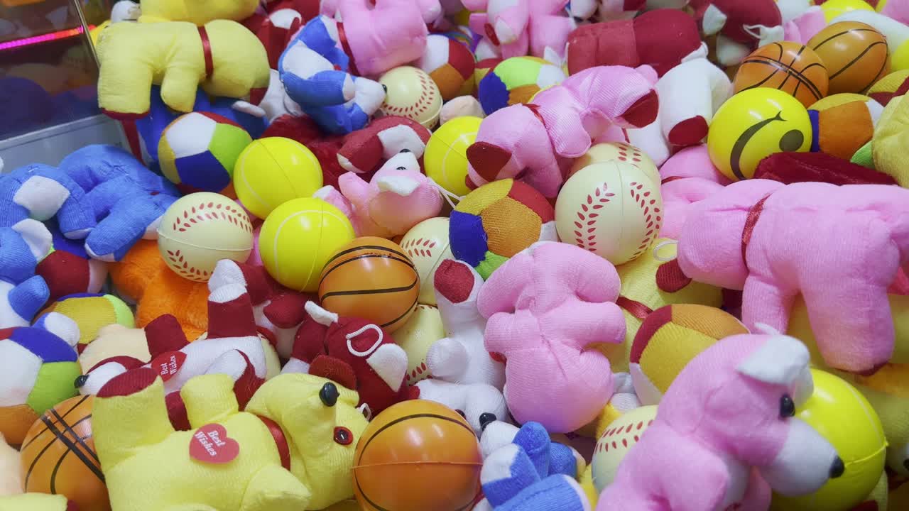 Tilt-up view showing a pile of plush toys and sports balls in bright colors inside an arcade machine, with a smooth upward movement capturing vibrant details and playful textures