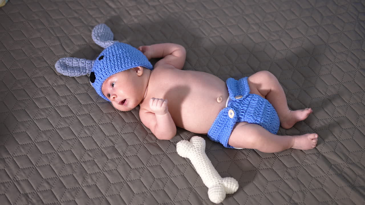 Funny baby boy wearing knitted suit of a puppy. Soft toy bone next to the babe. View from above.