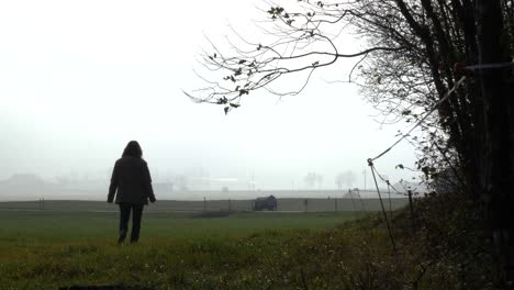 middle aged woman with a brown jacket walks over a green field of gras but suddenly stops and looking back