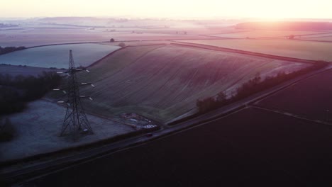 A-car-goes-along-a-road-underneath-a-pilon-during-a-frosty-winter-sunrise-sunset-English-countryside