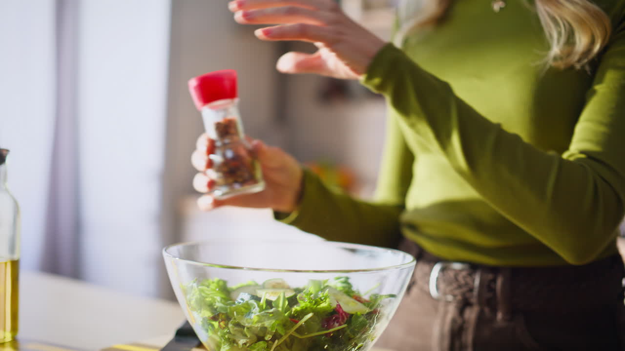 Primer plano de manos de mujer vertiendo aceite para hacer ensalada en casa. Señora desconocida preparando el almuerzo