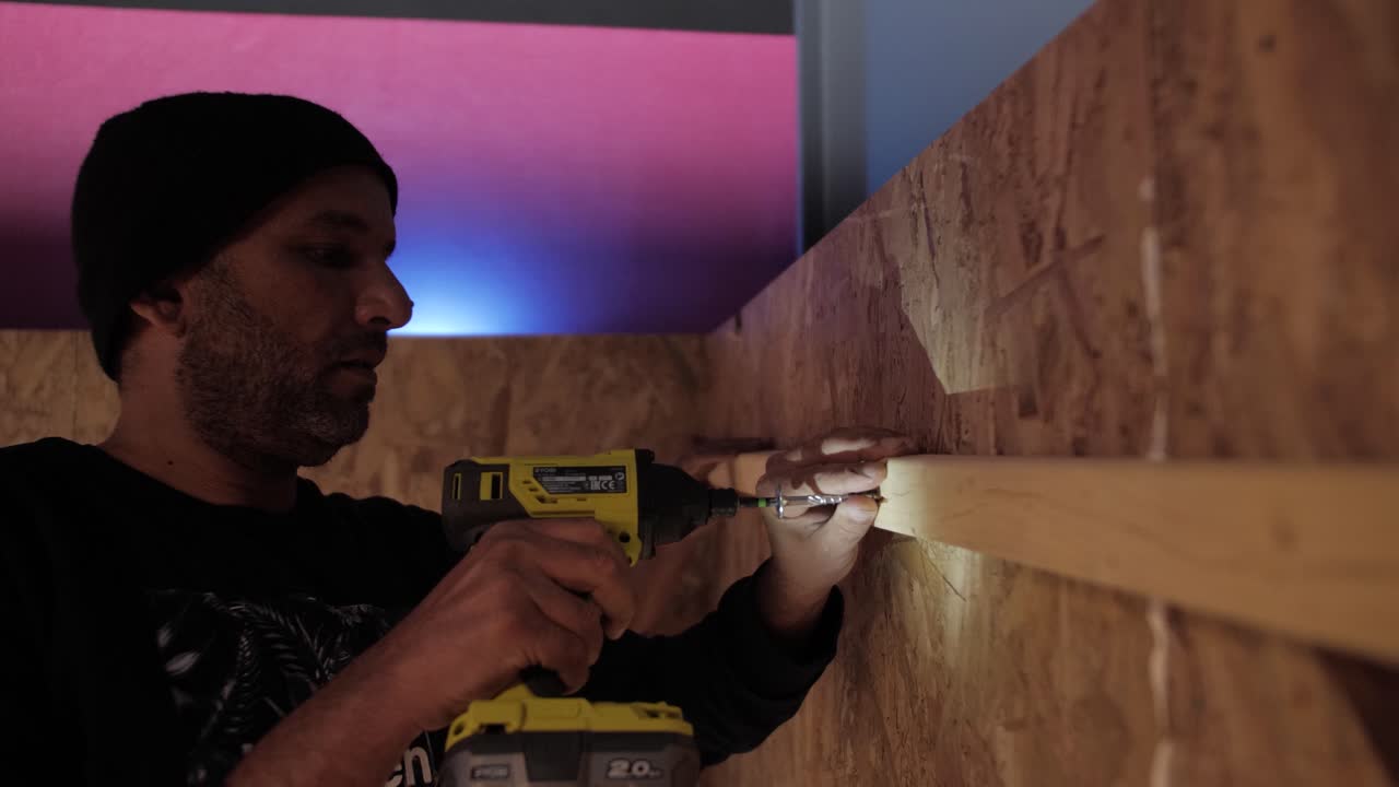 Focused worker drilling a wooden plank into a wall during indoor construction