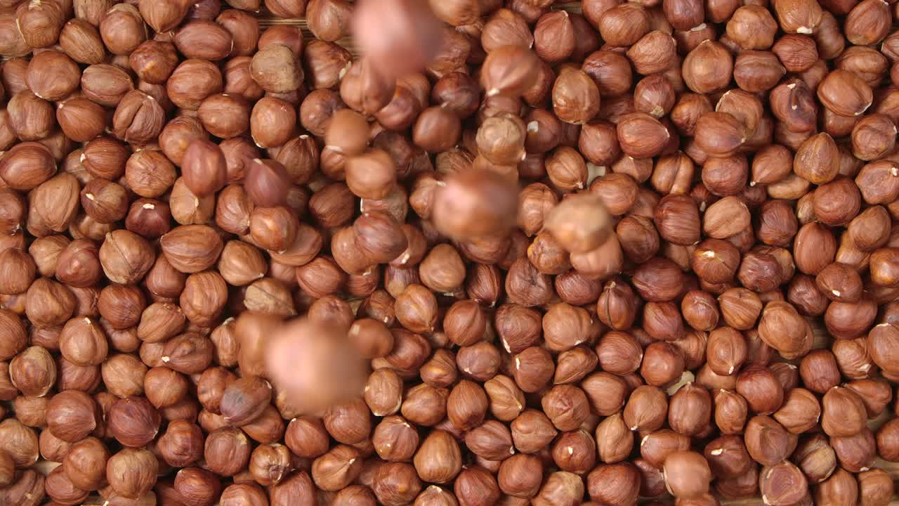 Nocciole marroni cadono su un mucchio di noci sgusciate. Vista dall'alto di nocciole in primo piano. Bellissimo sfondo di cibo biologico naturale. Slow motion.