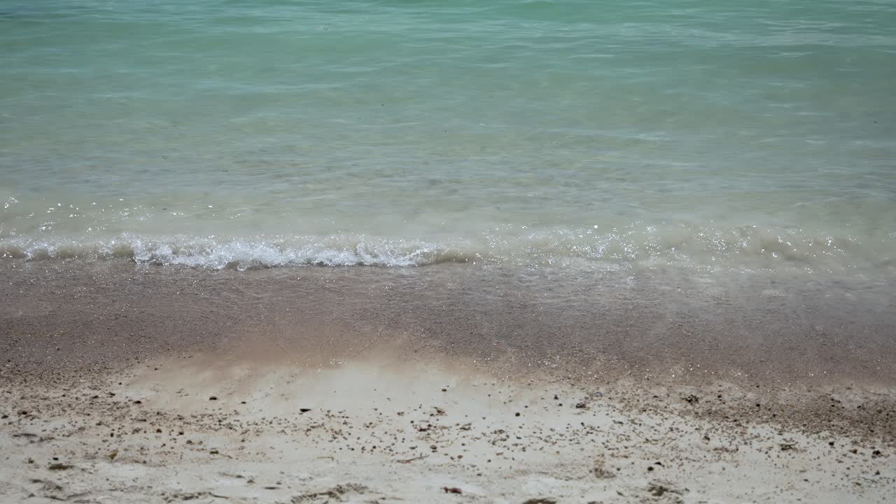 Glistening turquoise ocean water gently cascading onto pristine white sand beach. Creating foamy waves adding serenity to stunning seascape. Inviting relaxation and soaking in nature's beauty