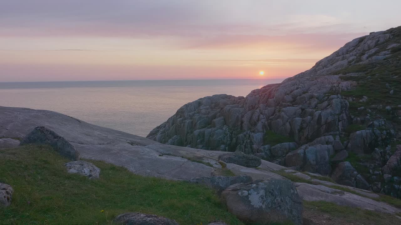 viendo desde la cima de un acantilado a lo largo de la costa hasta el horizonte, con vistas al océano tranquilo con una hermosa puesta de sol rosada y un cielo despejado