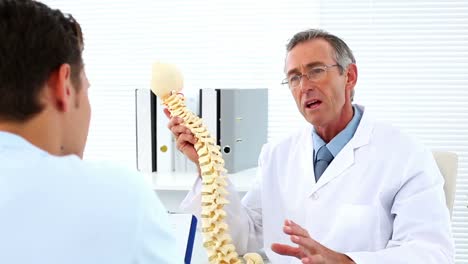 Mature-doctor-talking-to-his-patient-about-model-of-spine