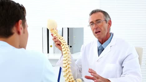 mature doctor talking to his patient about model of spine