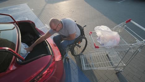 adult man with disabilities in a wheelchair puts purchases in the trunk of a car in a supermarket parking lot