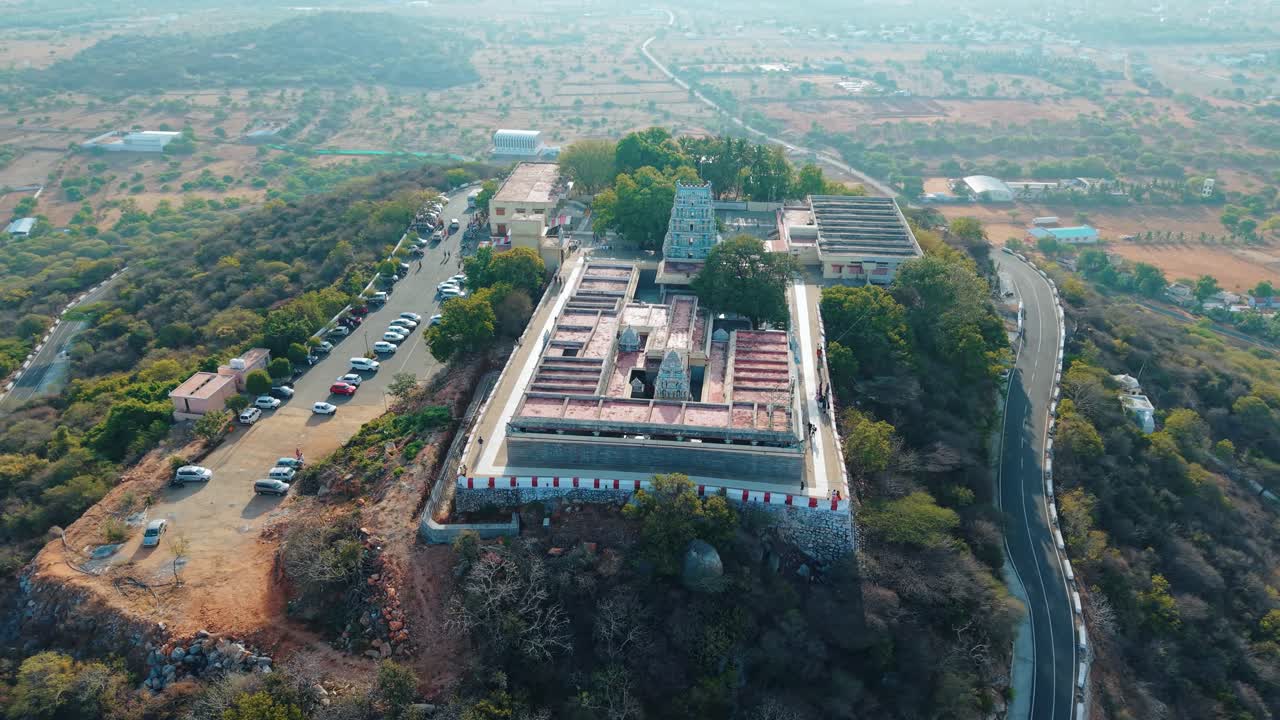 Vista aerea cinematografica del tempio di Sivanmalai, situato maestosamente in cima a una collina, circondato dal verde, con una strada di montagna tortuosa che aggiunge fascino a questo sereno punto di riferimento spirituale e panoramico