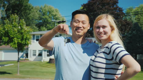 happy multi-ethnic couple on the background of their new home holds a key chain with keys in hand bu