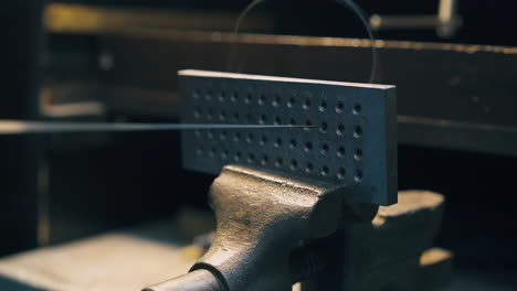 jeweler pulls gold wire through tool with holes close view