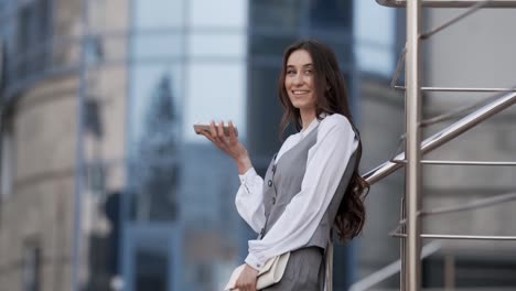 Cheerful-beautiful-young-woman-in-business-clothes-talking-to-a-smartphone