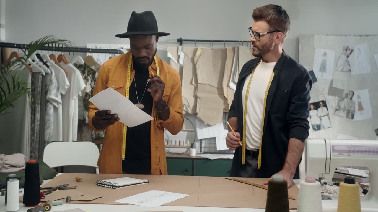 jóvenes y diseñadores de ropa trabajando juntos en una nueva colección, hablando y haciendo esquemas