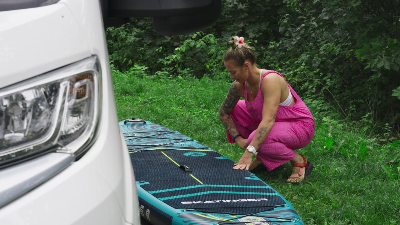 Una donna tatuata prepara un paddleboard gonfiabile (SUP) per pagaiare all'aperto. Inquadratura fissa.