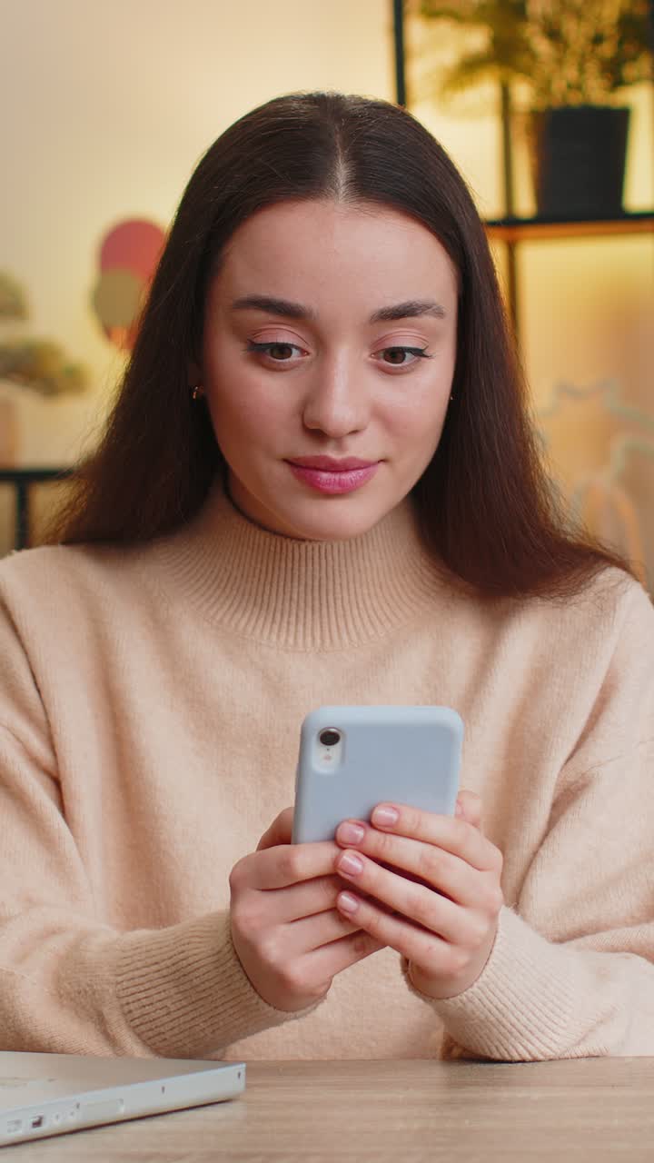 Donna caucasica al tavolo di casa usa lo smartphone celebra il successo la vittoria la vittoria gioca al gioco online