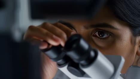 close-up of a person looking through a microscope in a laboratory
