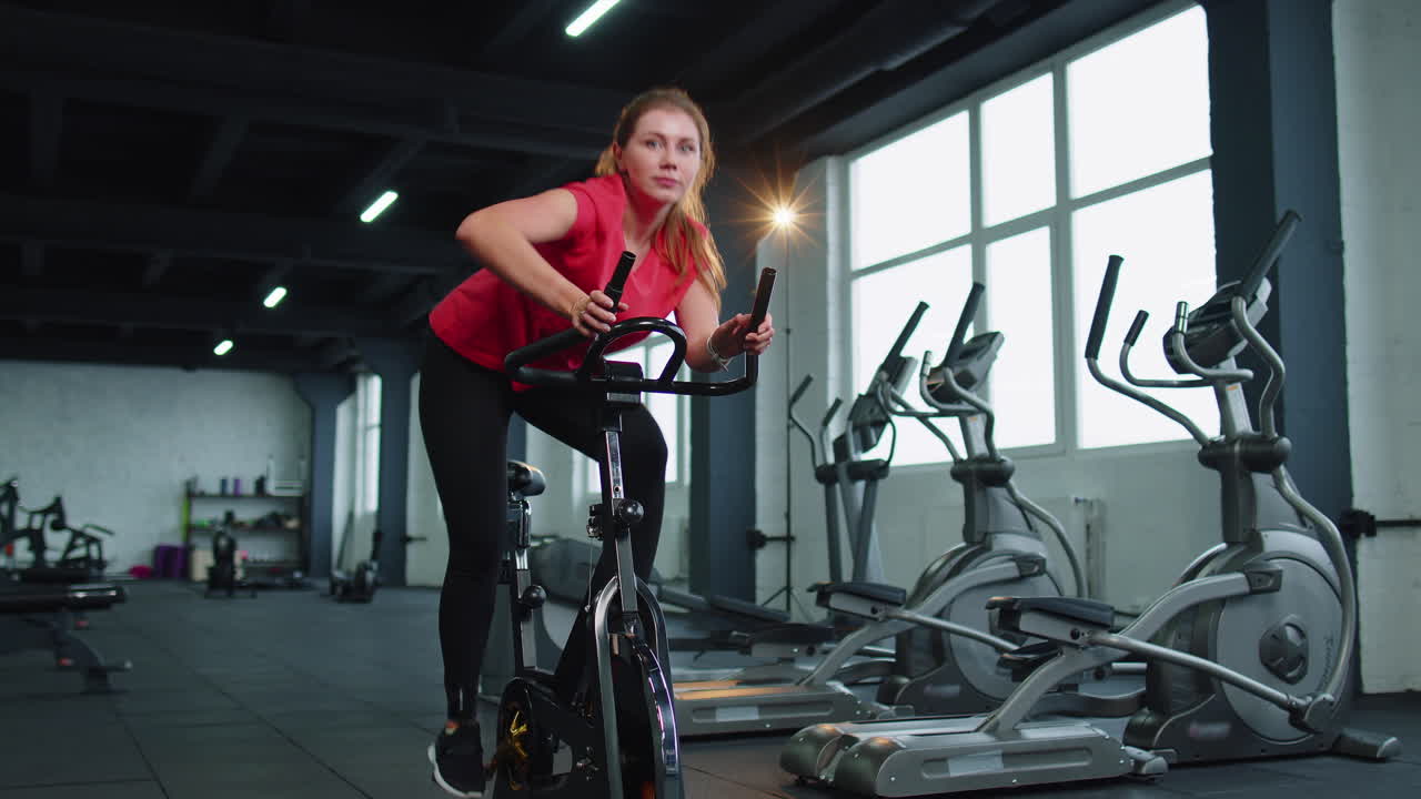 Lezione di gruppo di due amiche che si allenano, facendo spinning su cyclette in una palestra moderna.