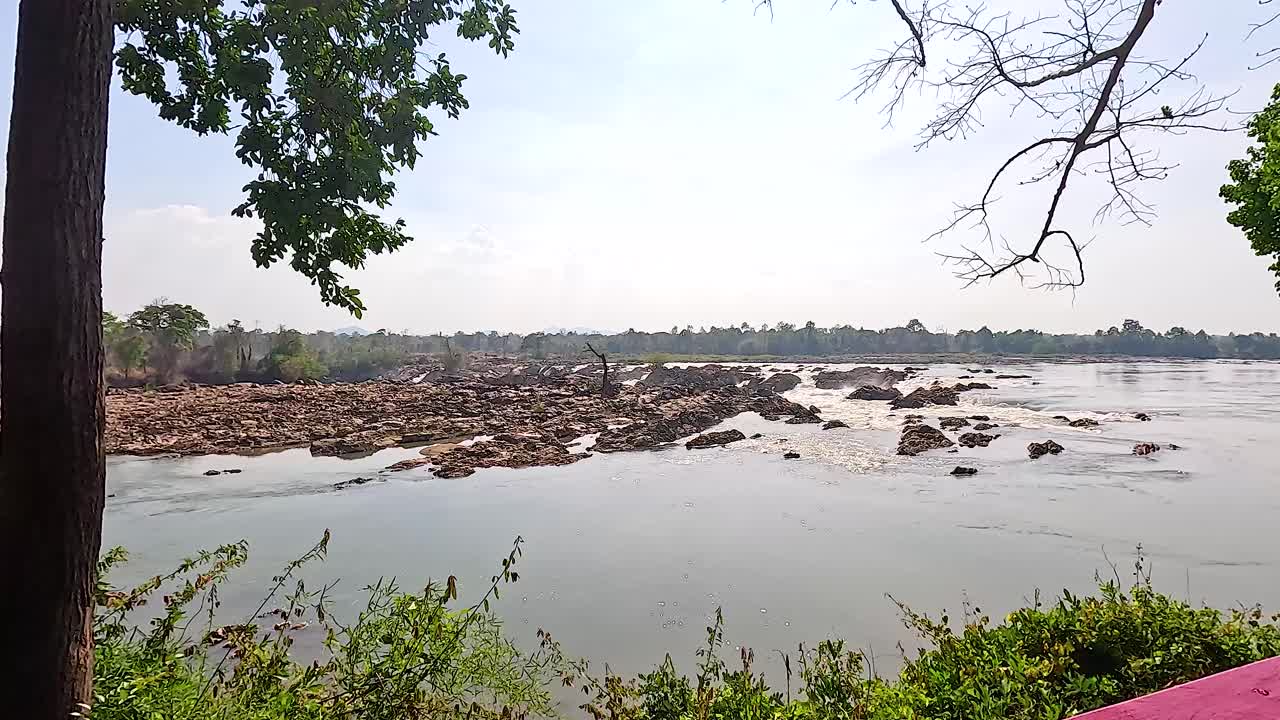 A tranquil scene of Khone Phapheng Falls with flowing water and lush greenery under soft daylight