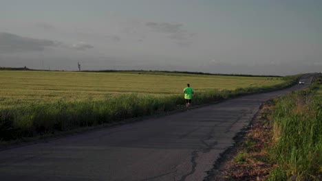 Hombre-En-Verde-Neón-Corriendo-Frente-A-La-Cámara-Y-Los-Campos-De-Trigo-En-La-Noche-De-Primavera