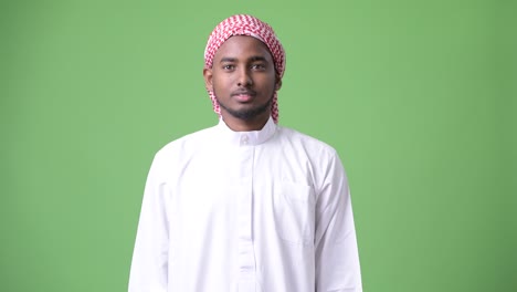 young handsome african man wearing traditional muslim clothes against green background