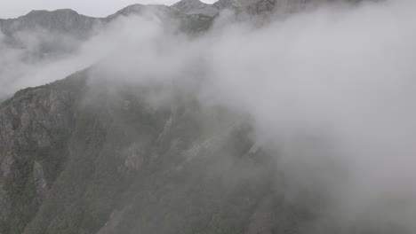 majestic mountain landscape with fluffy clouds rolling over, aerial drone view