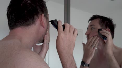 man shaving his beard in front of a mirror with an electrical razor