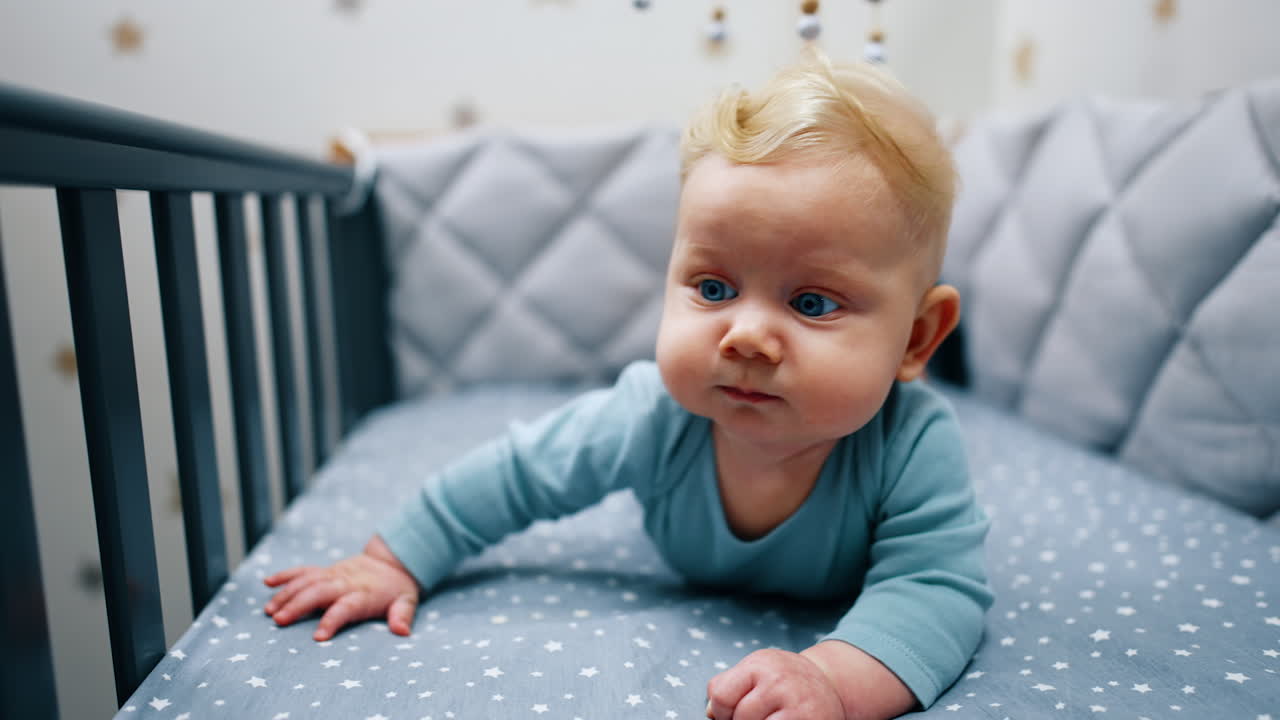 Adorable Caucasian child with big blue eyes and blond hair. Infant lies peacefully on his belly in the crib. Close up.