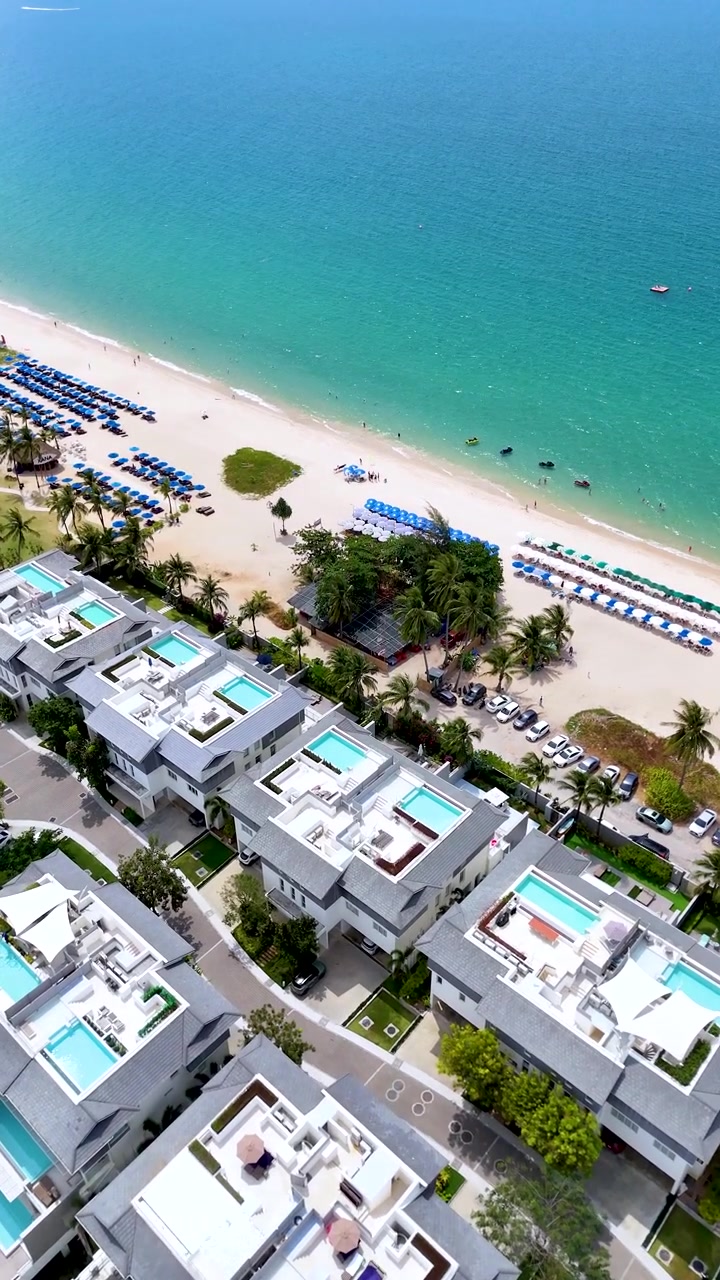 Toma aérea con dron que sobrevuela villas blancas modernas con piscinas privadas a lo largo de una costa tropical.