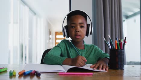 Portrait-of-african-american-boy-waving-and-doing-homework-looking-at-the-camera