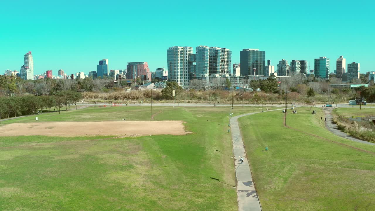 都市公園で歩いたりジョギングしたりする男性、草木が生い茂るタワーと建物、スカイライン、クレーンショット