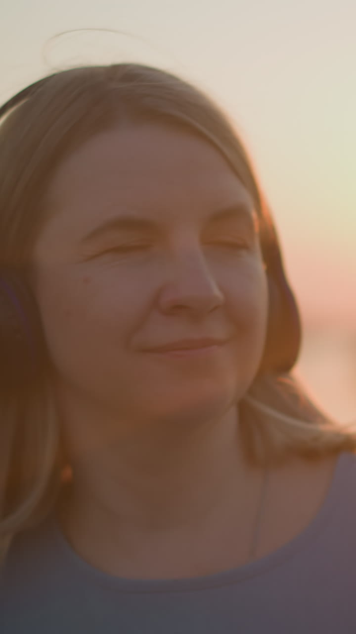 primer plano de una mujer con auriculares, sonriendo satisfecha mientras se baña en el cálido resplandor del sol poniente. los rayos del sol crean un efecto suave y dorado a su alrededor, añadiendo un ambiente pacífico