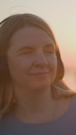 primer plano de una mujer con auriculares, sonriendo satisfecha mientras se baña en el cálido resplandor del sol poniente. los rayos del sol crean un efecto suave y dorado a su alrededor, añadiendo un ambiente pacífico