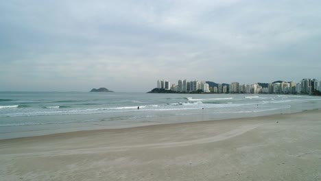 drone footage from the beach sand towards the calm and calm sea, buildings in the background and cloudy weather, brazil beach, guaruj?