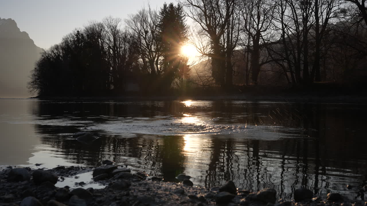 Sunset light filtering through trees over calm Walensee lake in Switzerland