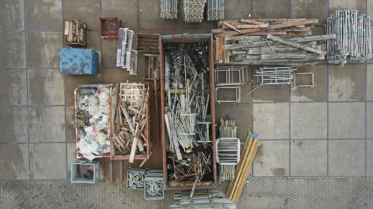 Top down aerial of wood and metal materials sorted in containers for recycling. The drone ascends and reveals a large industrial work yard