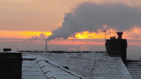 smoking industry chimney above icy winter home rooftops glowing sunrise orange sky