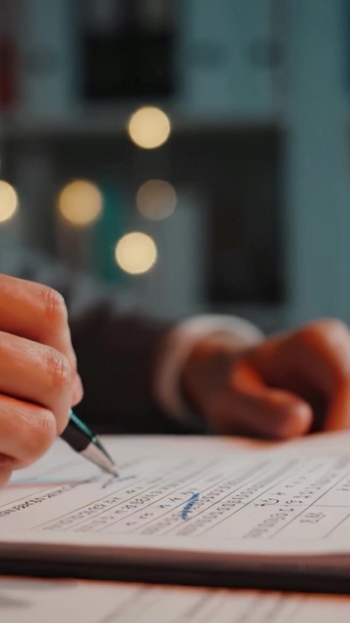 Persona che firma un documento con una penna in un contesto professionale, focus su mano e documenti legali con luci di sfondo sfocate che esaltano l'atmosfera di intento commerciale
