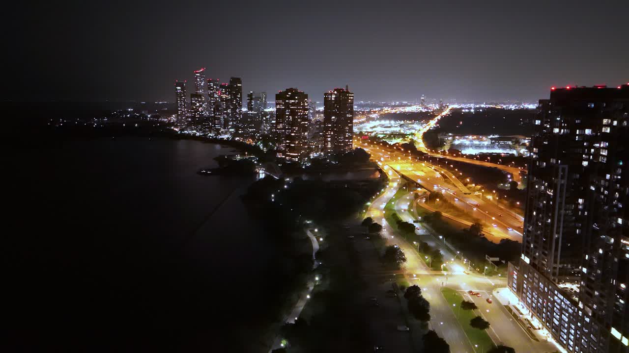 Drone shot at night over Lake Ontario showing Parklawn waterfront and illuminated skyscrapers