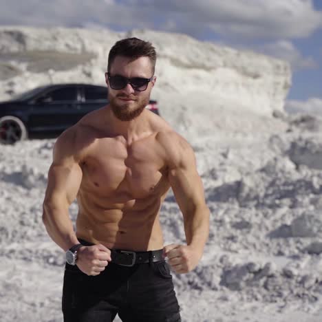athletic man posing on camera. strong bodybuilder without shirt shows his trained body on white canyon background. muscular sportsman outdoors.