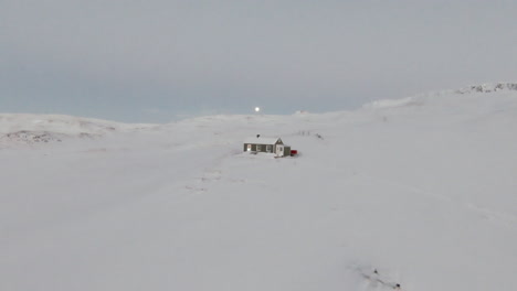 cabin in middle of snowy mountains with full moon in background