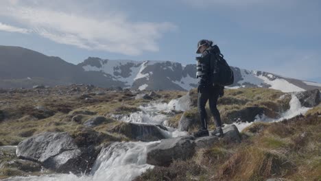 Woman-Arriving-at-Waterfall-and-Taking-in-Beautiful-Scenery-Surrounded-by-Scotland-Mountains-on-Clear-Day