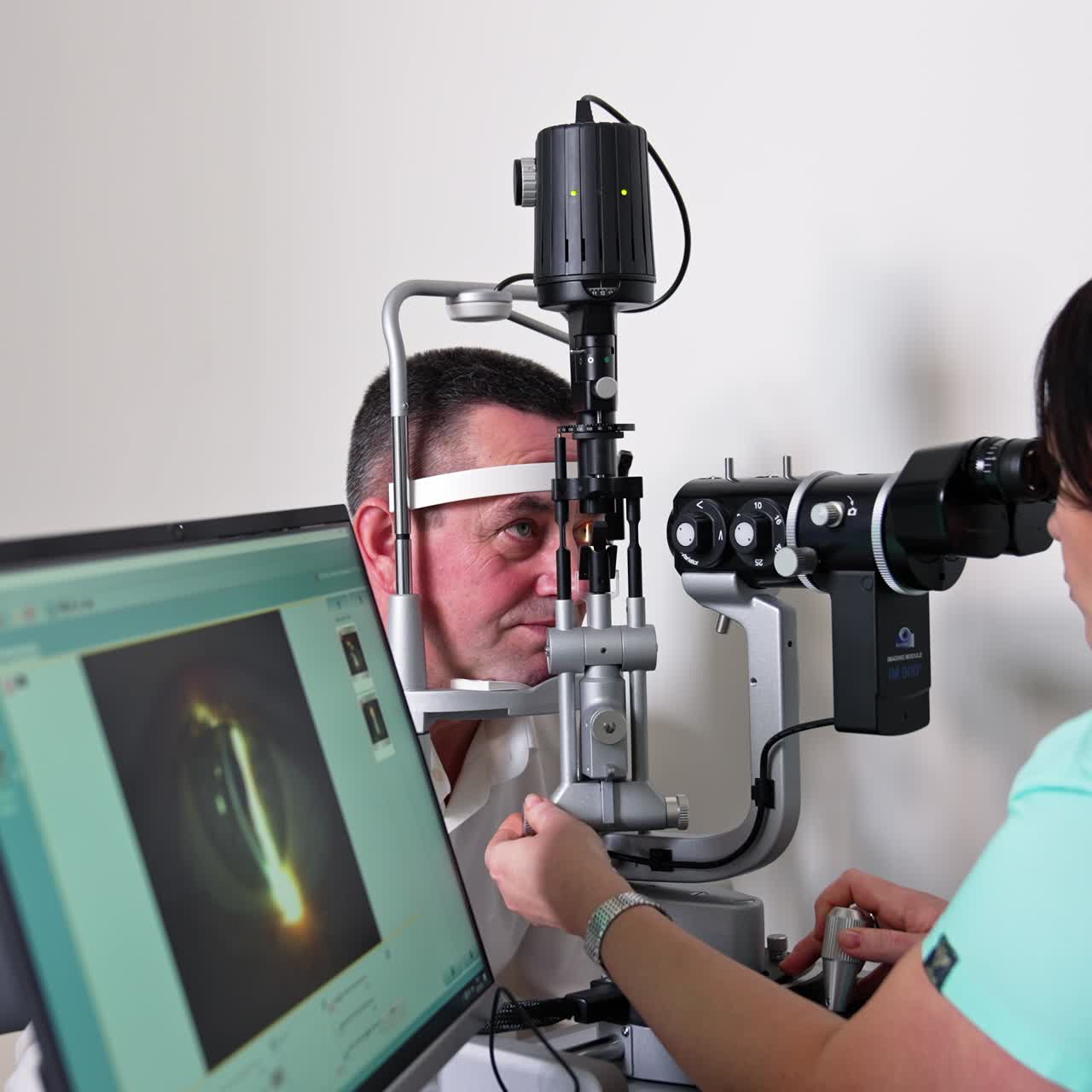 Adult man at ophthalmologist's examination. Female doctor check's male eyesight at deice, looking at the screen of computer