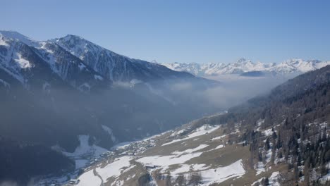 aerial drone shot of navistal, tyrol: green meadows on the sunny side, snowy peaks above. a stunning spring landscape showing winter’s transition