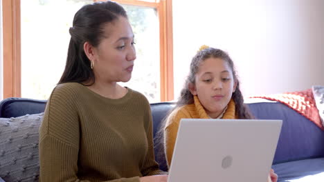 Glückliche-Biracial-Mutter-Und-Tochter-Sitzen-Auf-Dem-Sofa,-Mit-Laptop-Und-Reden-Im-Sonnigen-Wohnzimmer