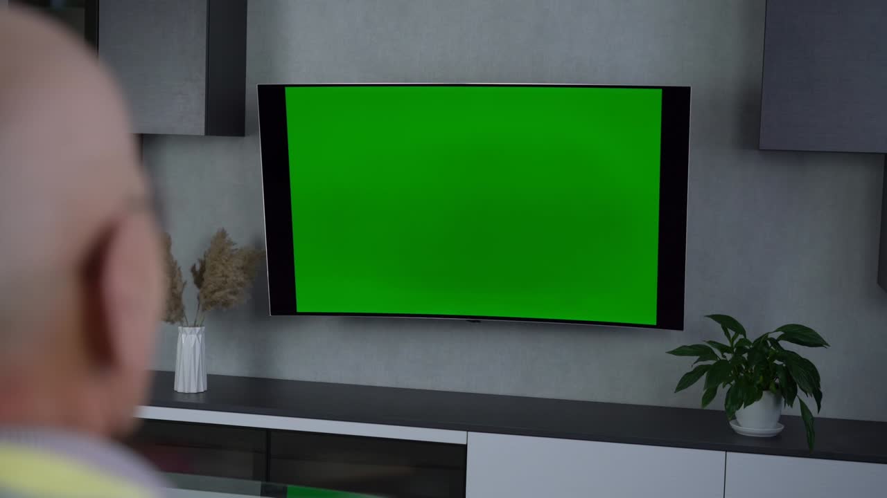 Older man watching sports broadcast on blank tv screen sitting on sofa at room