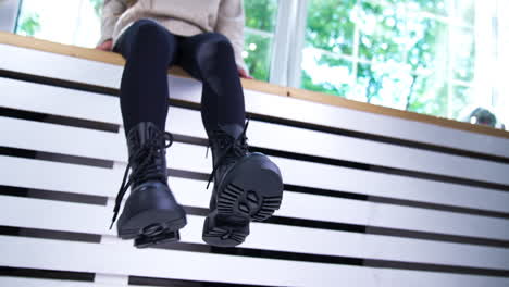 black boots with laces on tractor soles. close up. female model sitting on a window sill demonstrating fashionable footwear. low angle view.