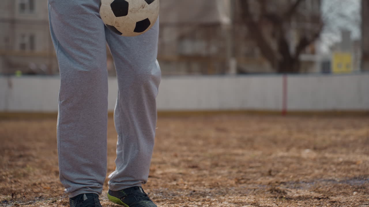 Primer plano de unos pies controlando el balón en un campo seco, ejercicio de regate con suelo texturizado y zapatillas de deporte informales; secuencia de juego de pies centrada, práctica deportiva a bajo ángulo, ideal para tutoriales y deporte a cámara lenta