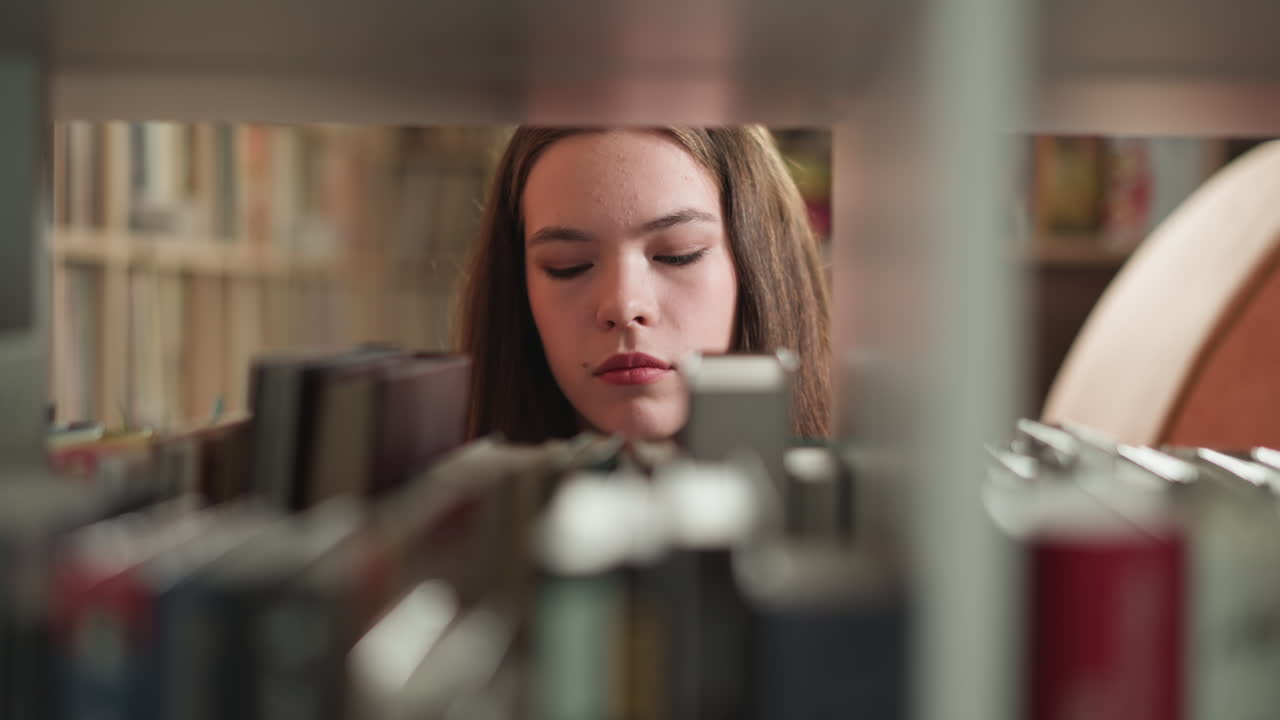 una mujer escanea una estantería en busca de libros. una lectora busca literatura emocionante en la estantería de la biblioteca de la universidad. una mujer en el almacén de libros