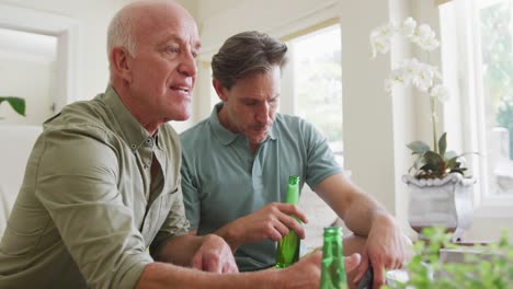 Happy-caucasian-grandfather-and-adult-son-watching-tv-and-supporting-in-living-room